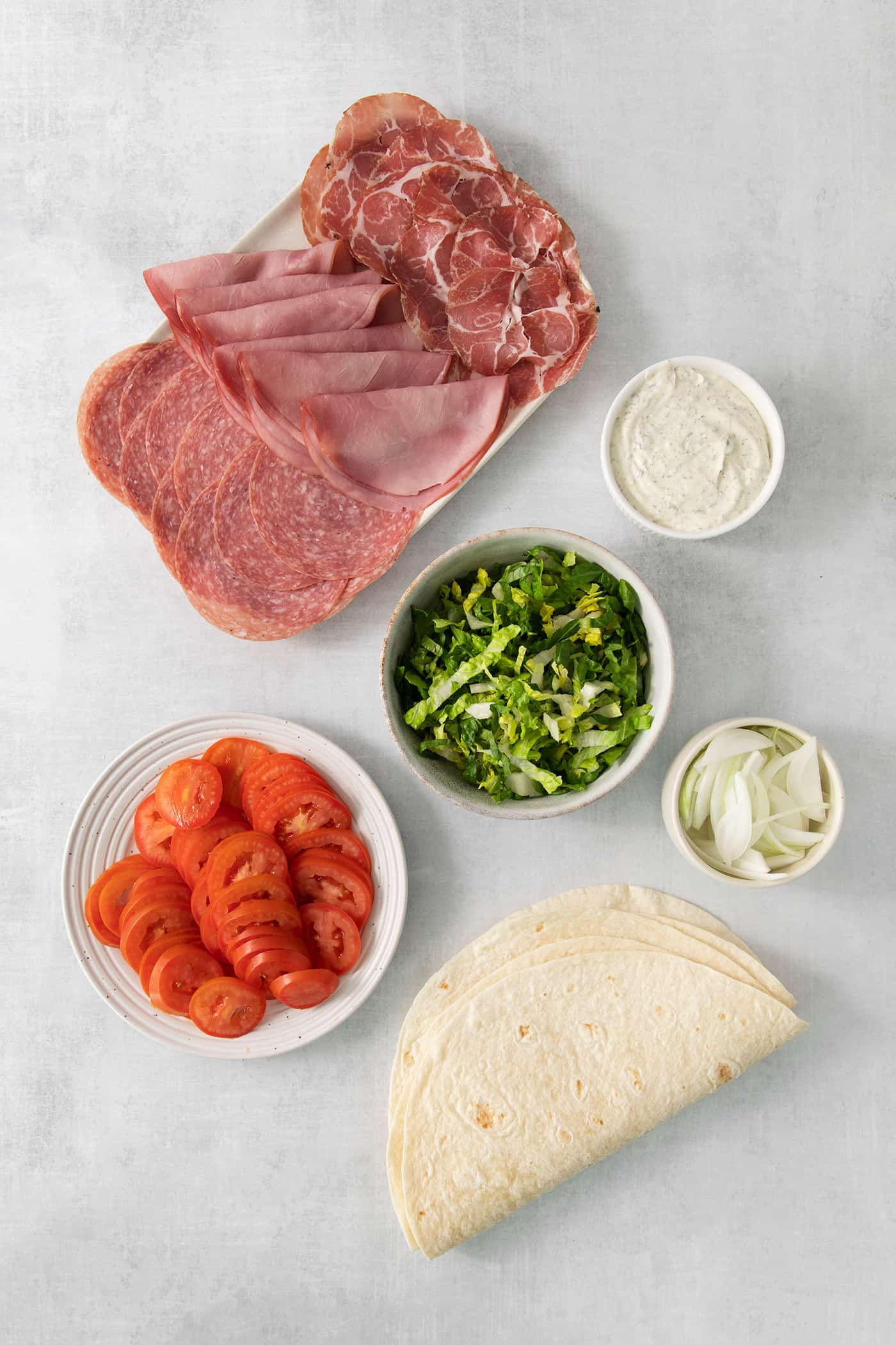 Ingredients for Italian pinwheels: meat, tomatoes, lettuce, cheese, and tortillas.