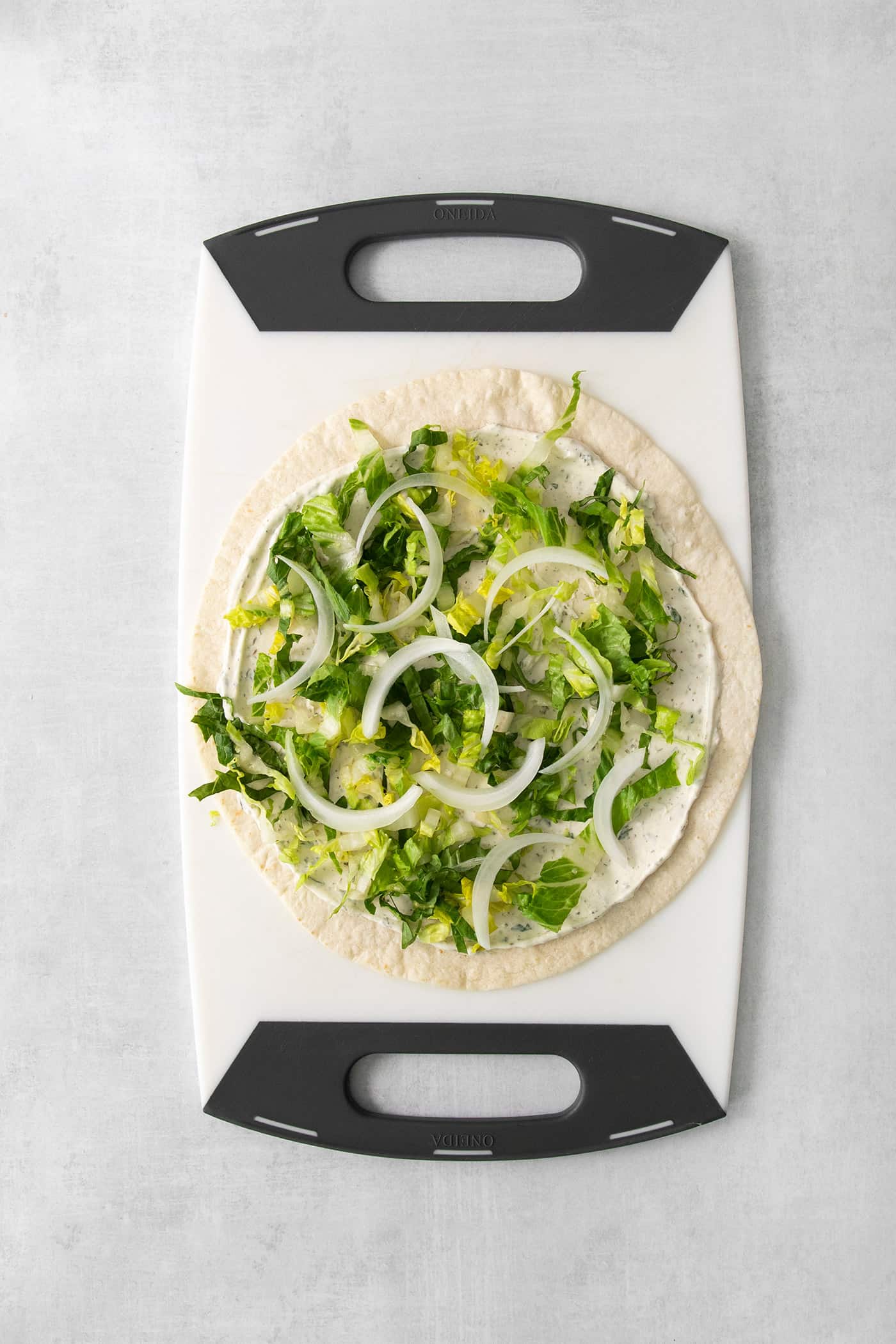 Now chopped lettuce and onion are added to the tortilla on a cutting board.