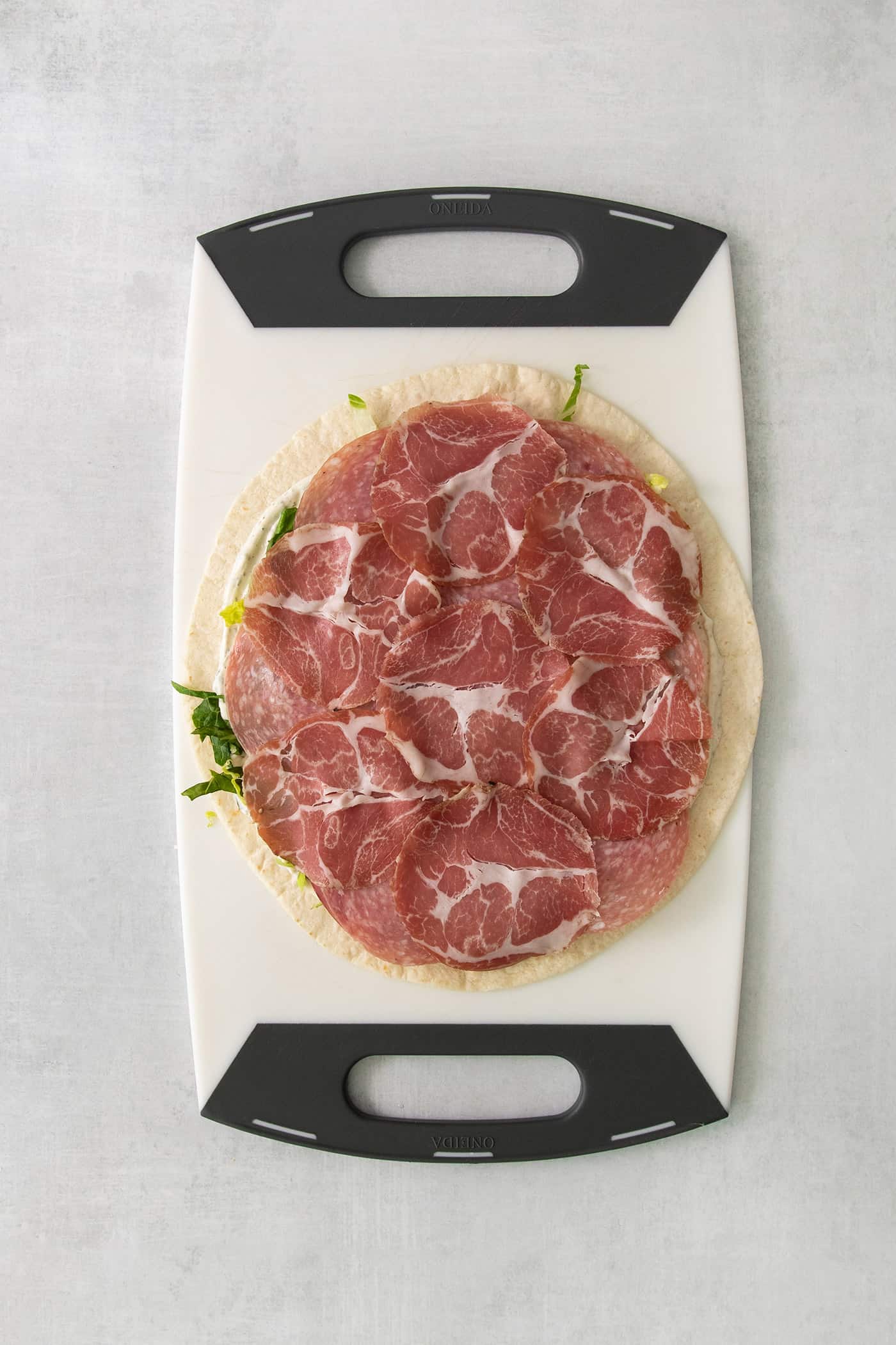 Meat is assembled on a cutting board to make Italian pinwheel sandwiches.