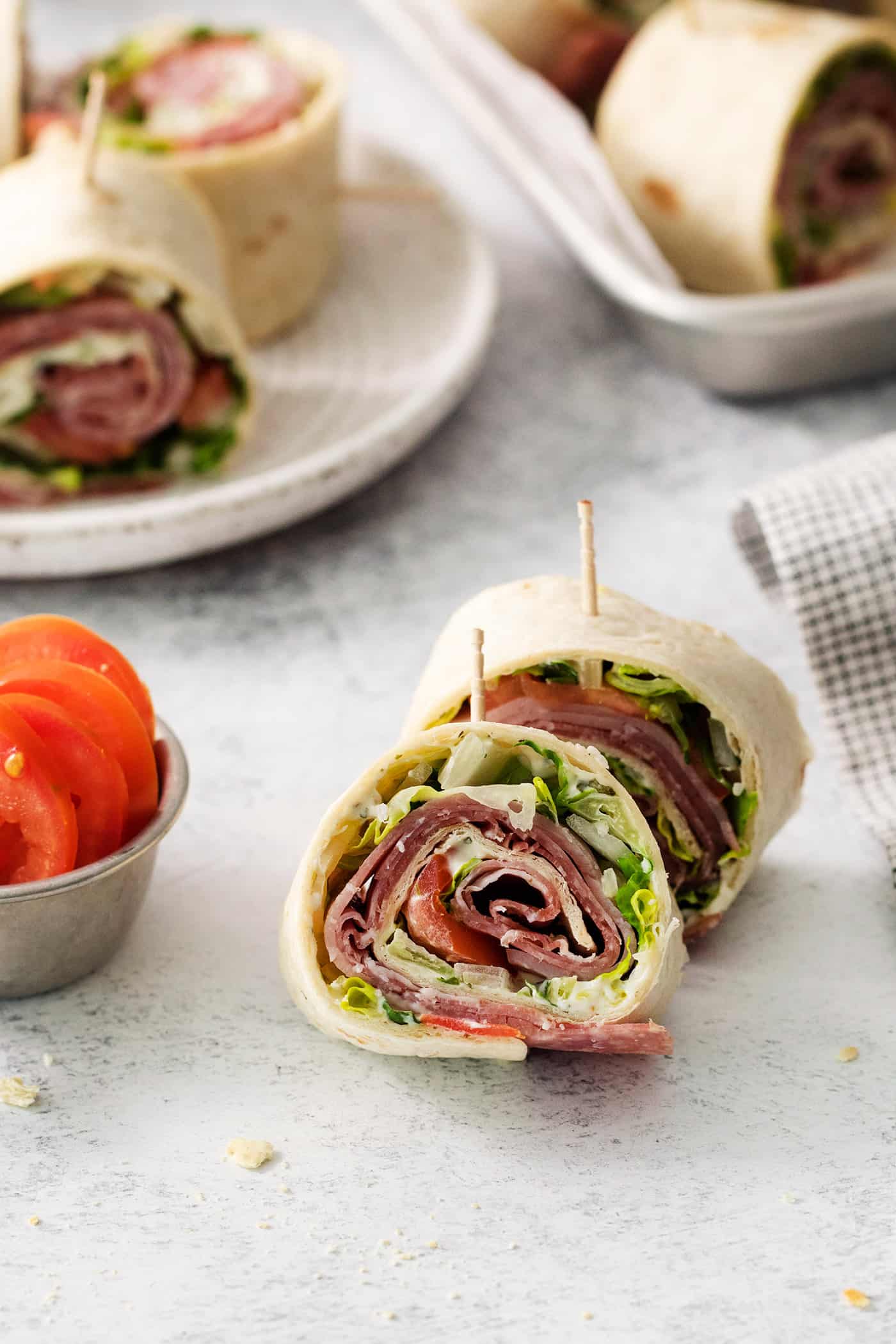 Italian pinwheels are shown on a white background with more in the back on a plate.