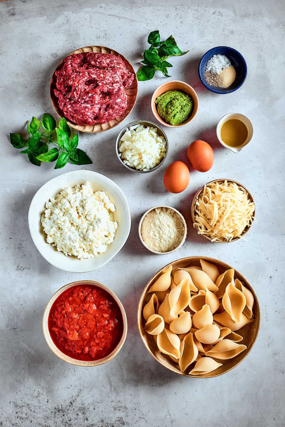 Ingredients for stuffed shells with meat are shown: eggs, pasta, cheeses, tomato sauce, spices, and meat.