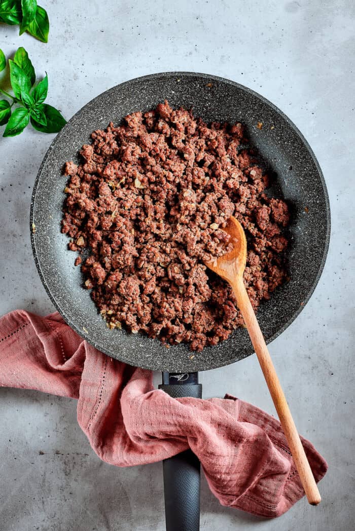 Cooking a pan of ground beef with a wooden spoon.