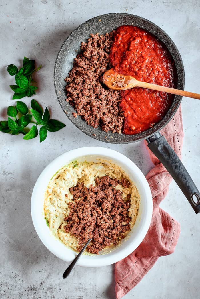 Ground beef is combined with tomato sauce in a skillet with a wooden spoon.