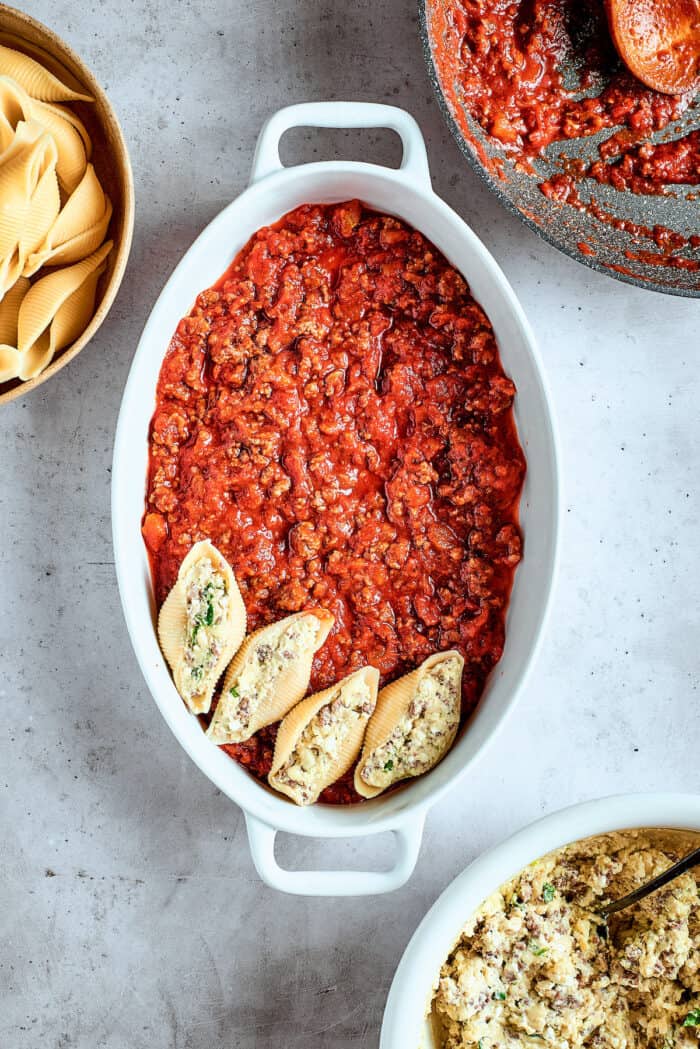 Arranging stuffed shells in a pan on top of marinara sauce.