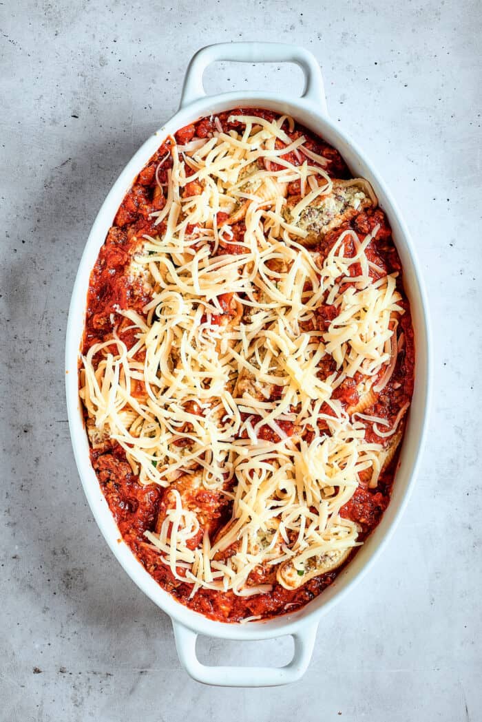 Shredded cheese tops a pan of stuffed shells with meat.