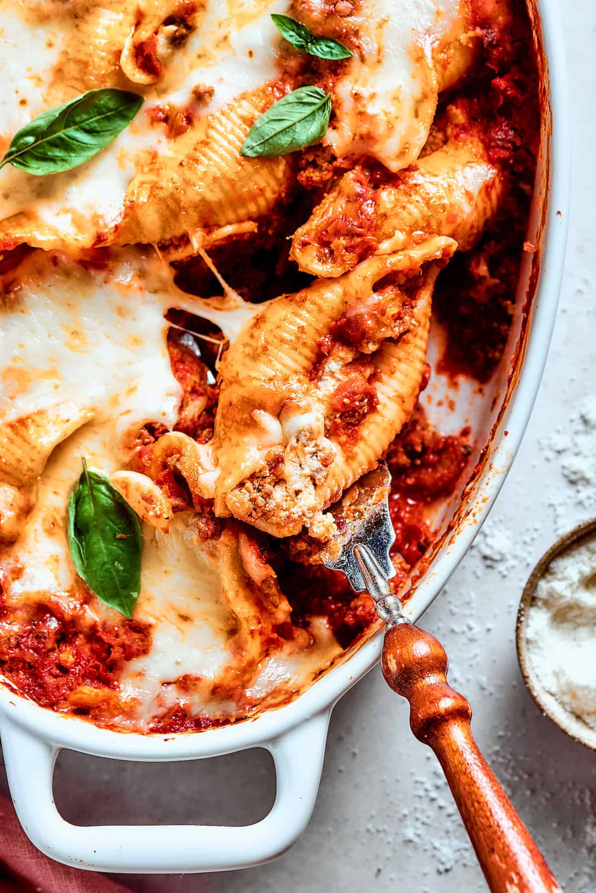 A serving utensil lifts out a stuffed shell with meat from the pan.