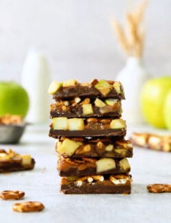 A stack of caramel apple bark with pretzels with apples in the background.