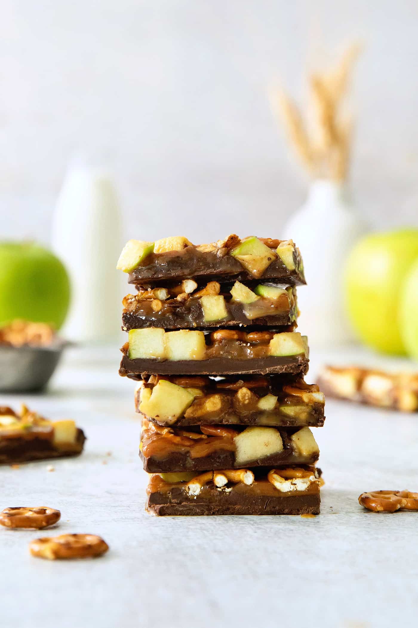 A stack of caramel apple bark with pretzels with apples in the background.