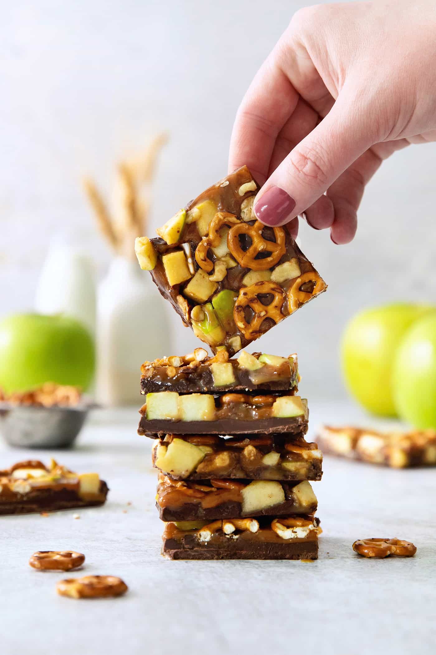 A hand lifts up a piece of caramel apple bark from a stack of bark.