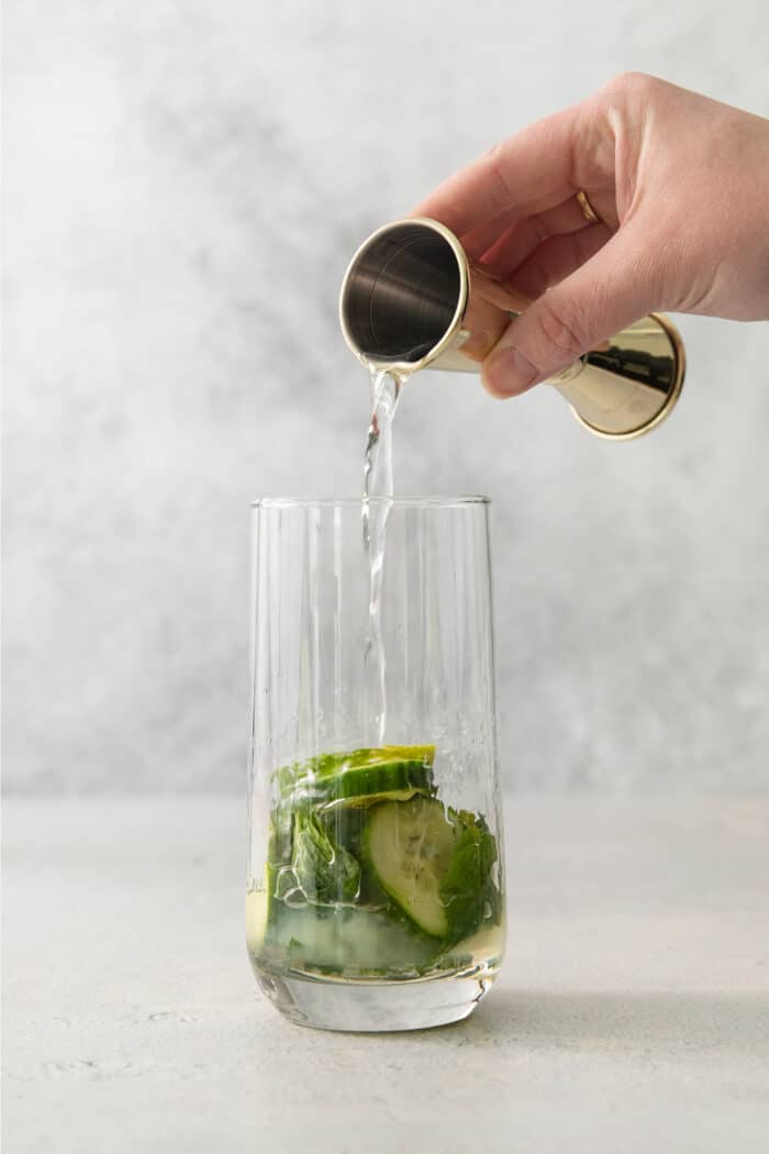 A hand pours in orange liqueur for a cucumber mojito.