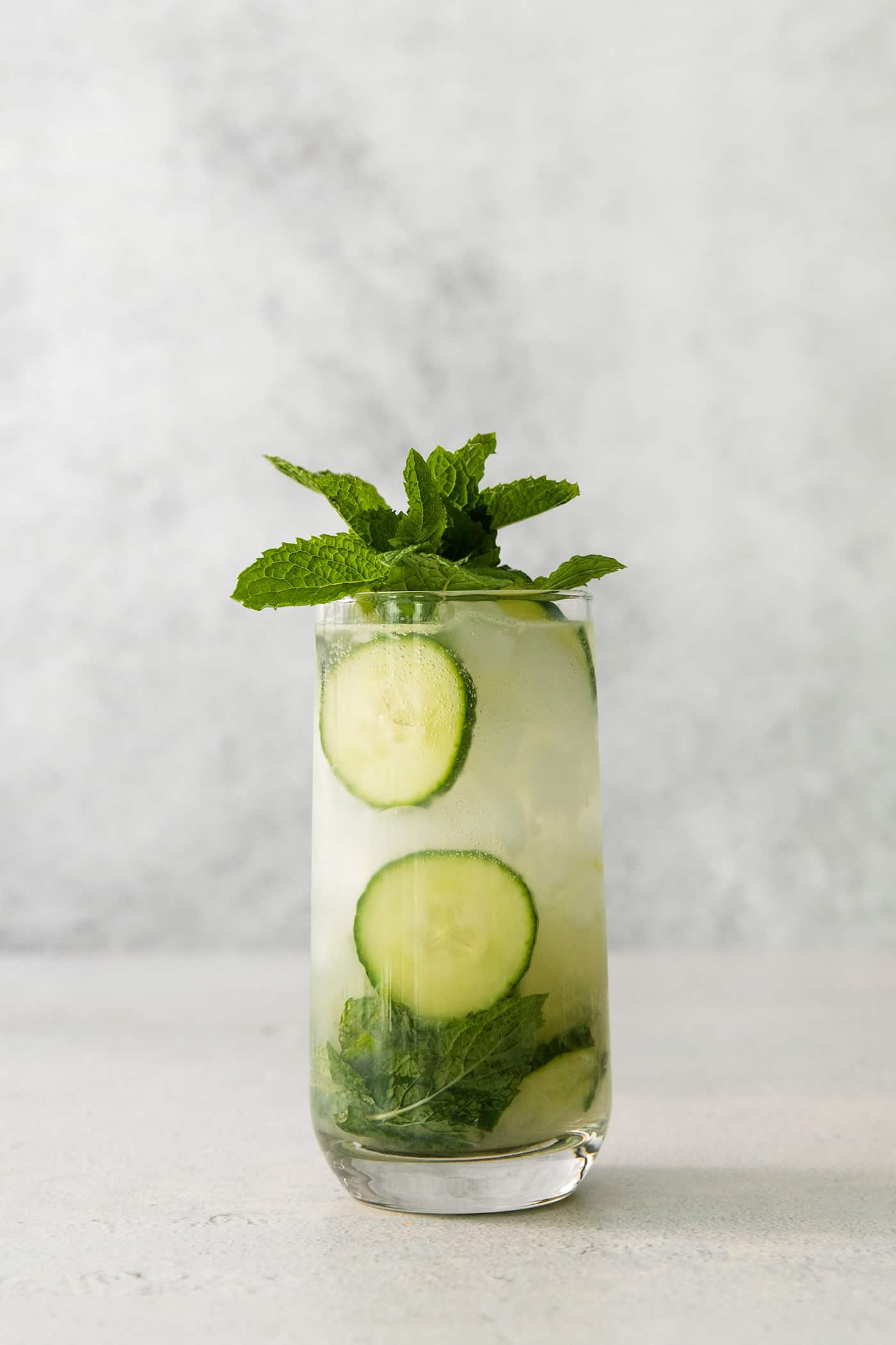 A glass of cucumber mojito topped with basil leaves.