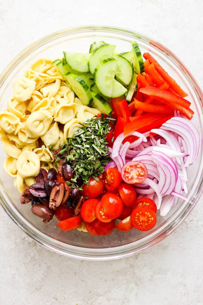 Ingredients for Greek tortellini salad are shown in a glass bowl.