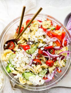 A bowl of Greek tortellini salad with serving spoons.
