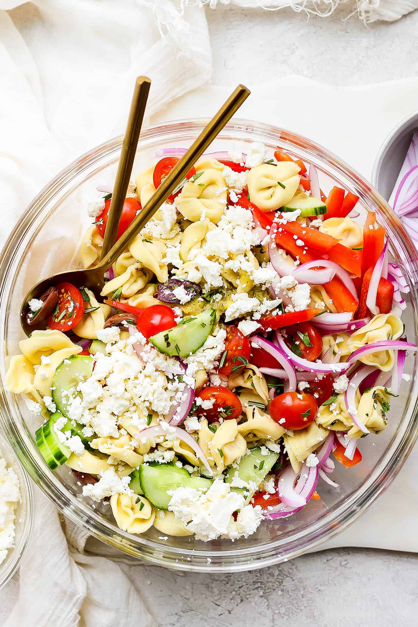 A bowl of Greek tortellini salad with serving spoons.