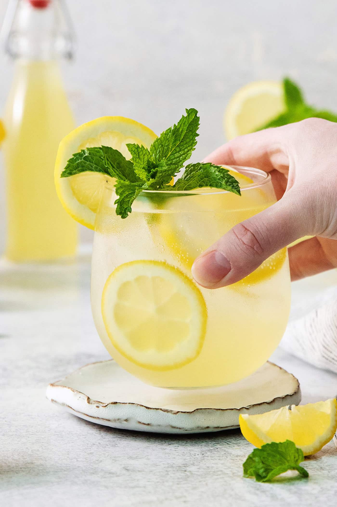 A hand holds a glass of limoncello spritz garnished with mint.