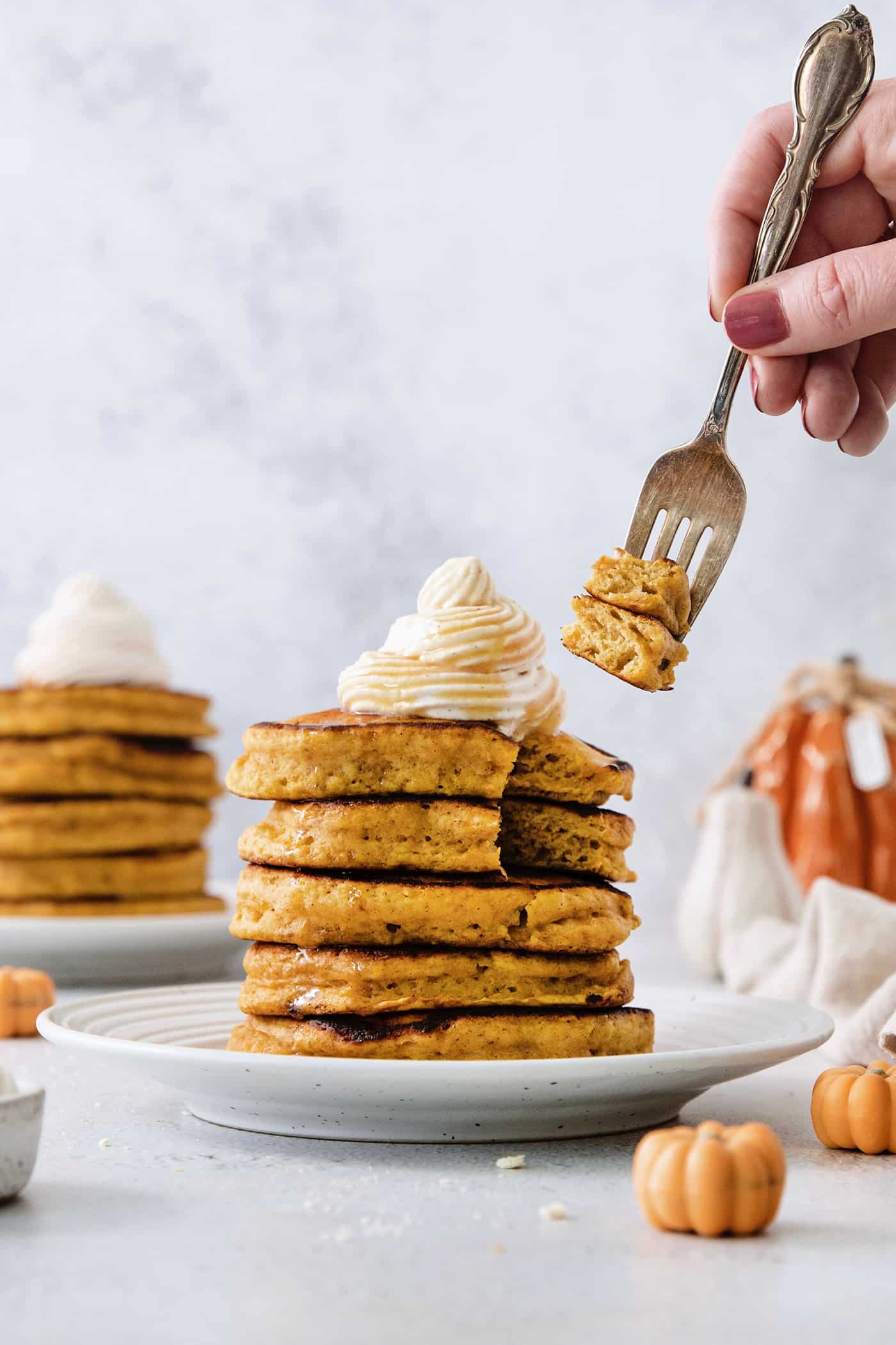 A fork holds pieces of pumpkin pancakes cut out of a stack of pancakes with more pancakes in the background.
