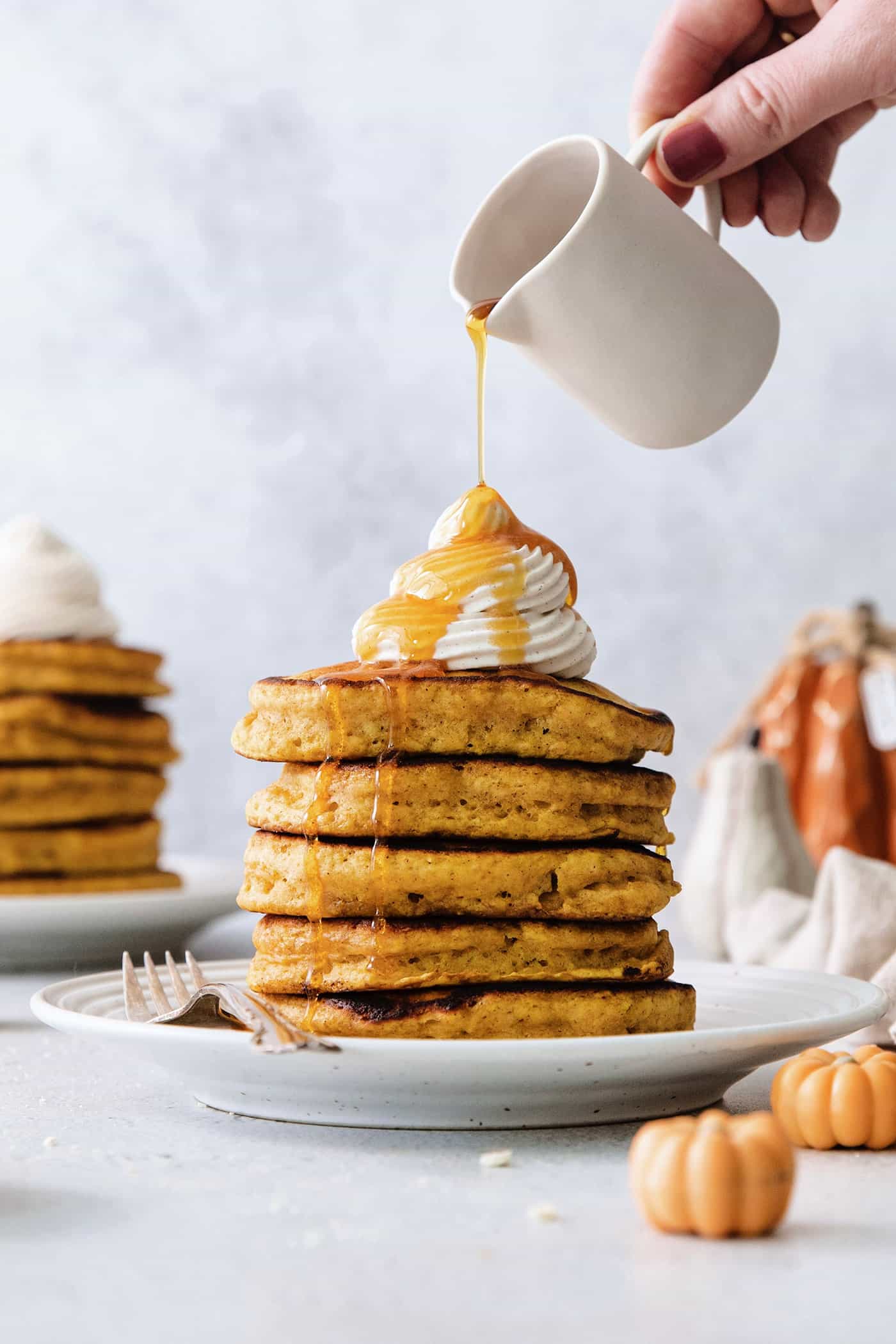 Maple syrup is poured over a stack of pumpkin pancakes with mini pancakes scattered around the plate.