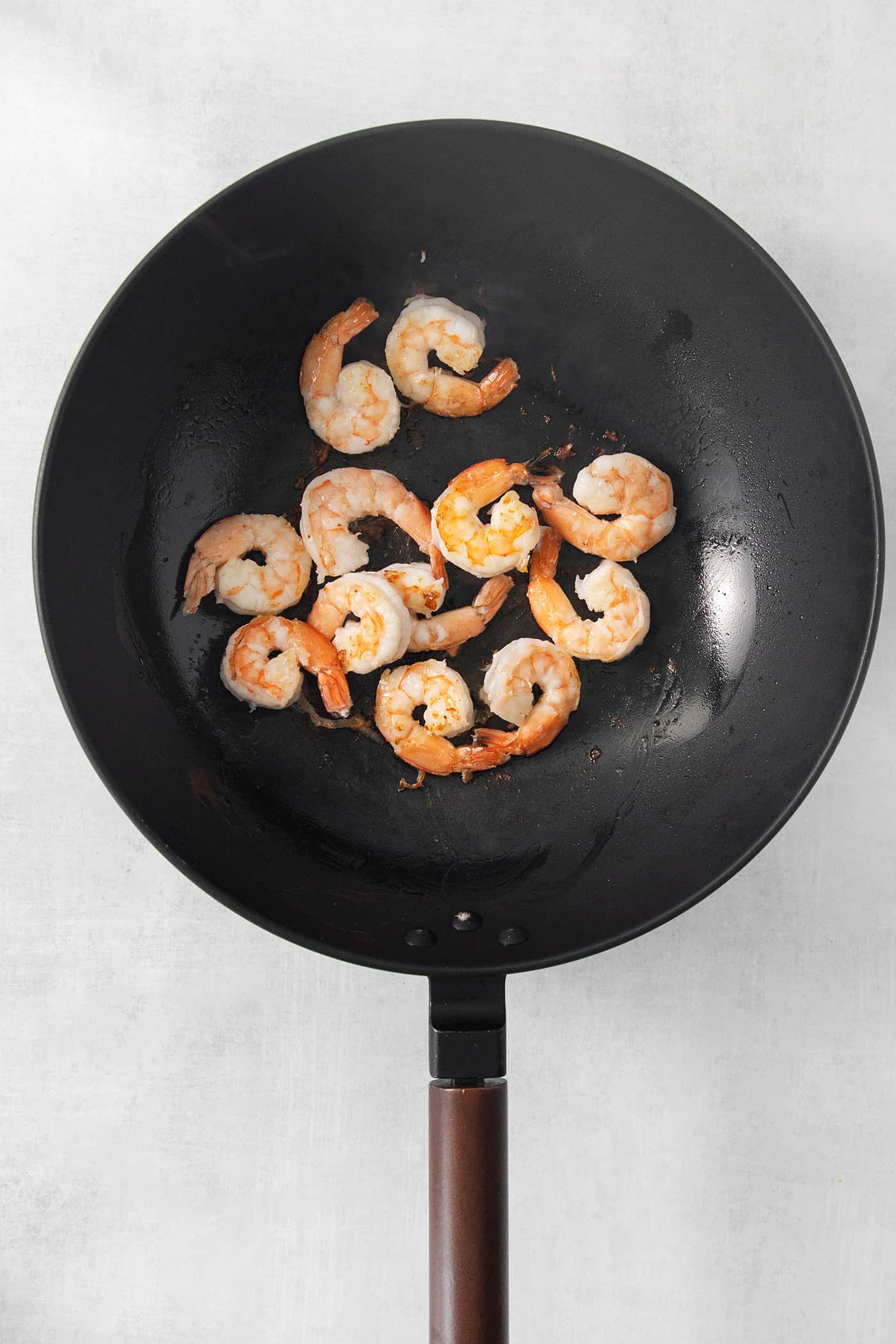 A black skillet in which shrimp cooks.