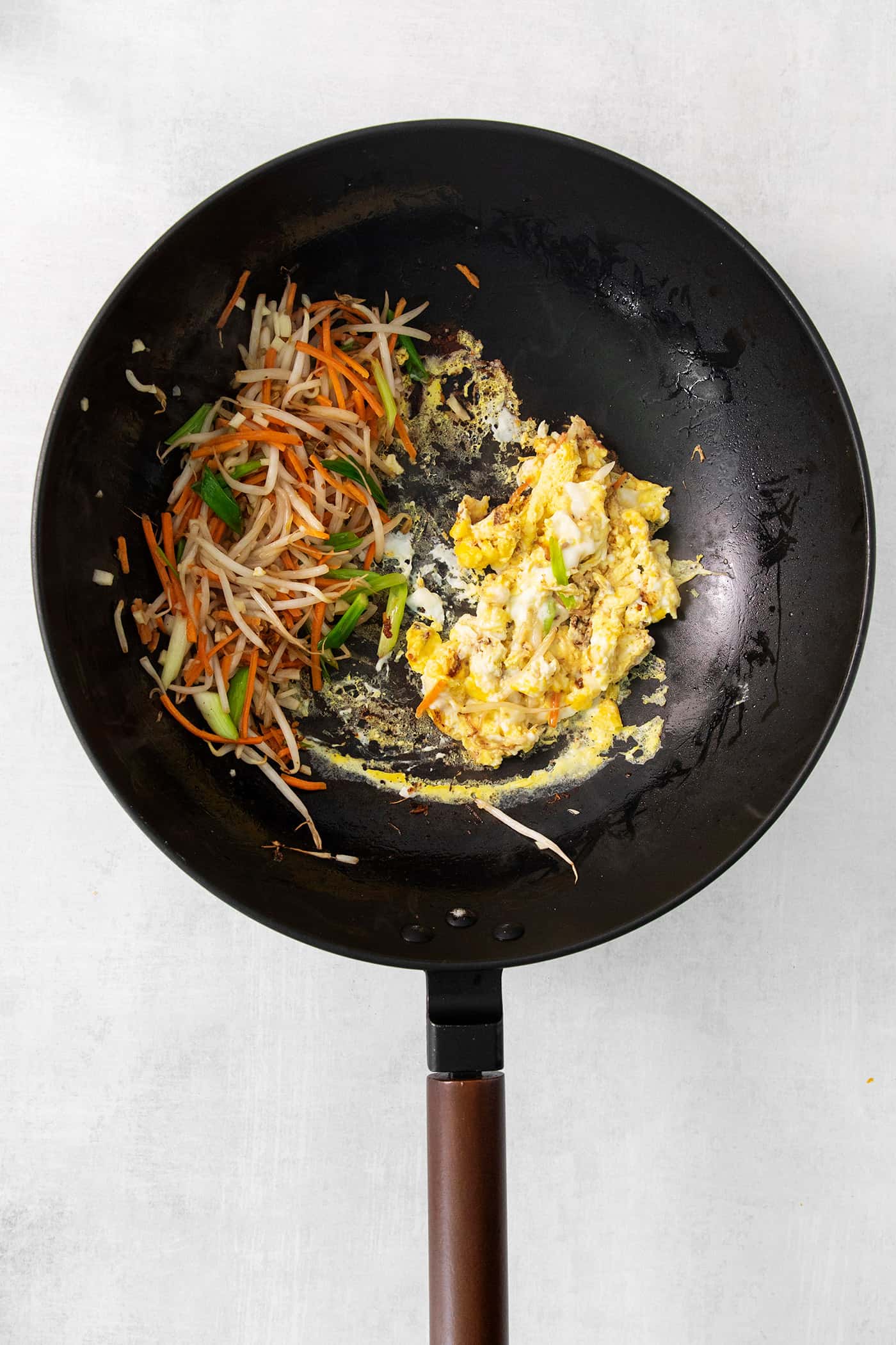 Scrambled eggs and vegetables cook in a black skillet for shrimp pad Thai.