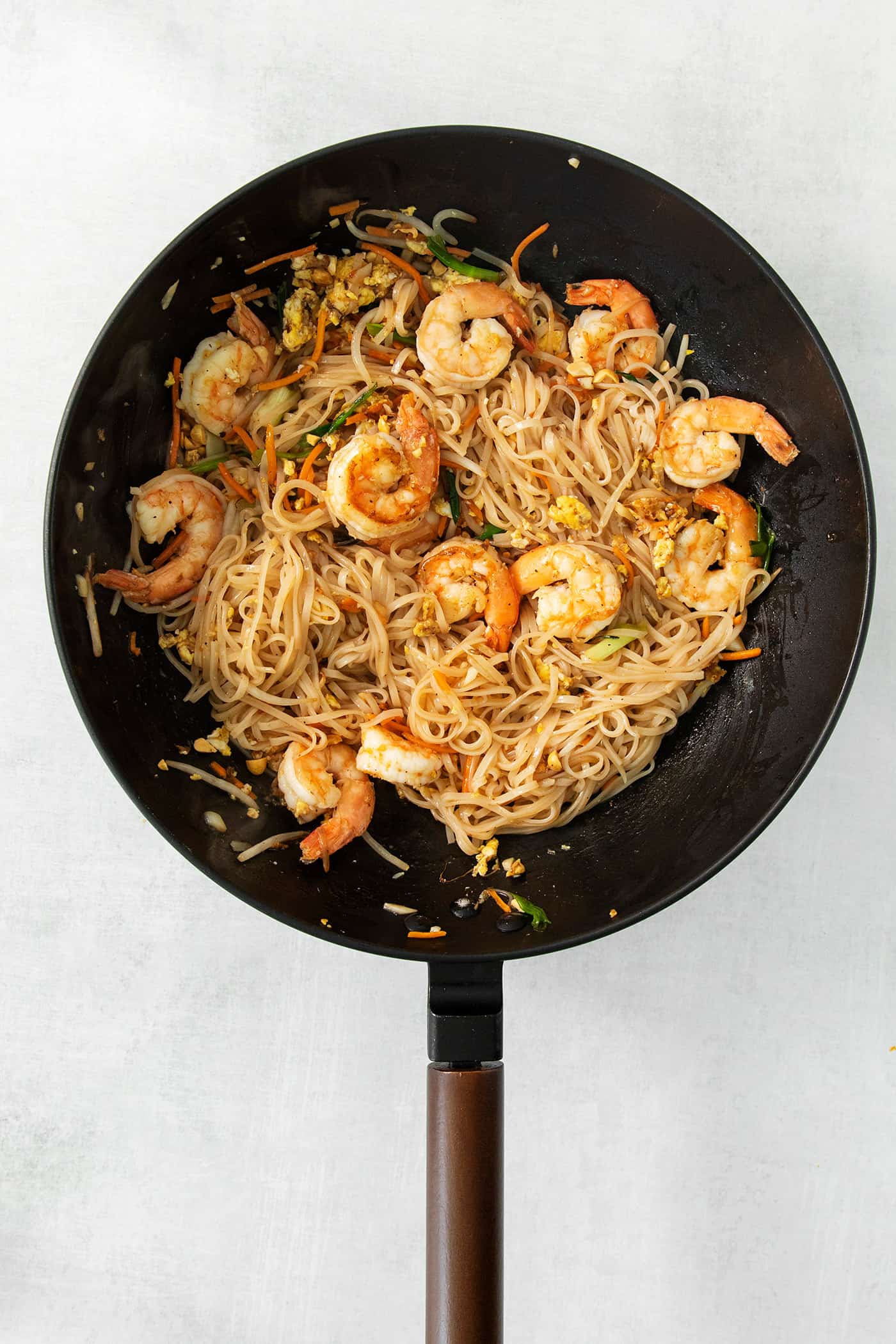 A skillet full of noodles, vegetables, and shrimp for shrimp pad Thai.