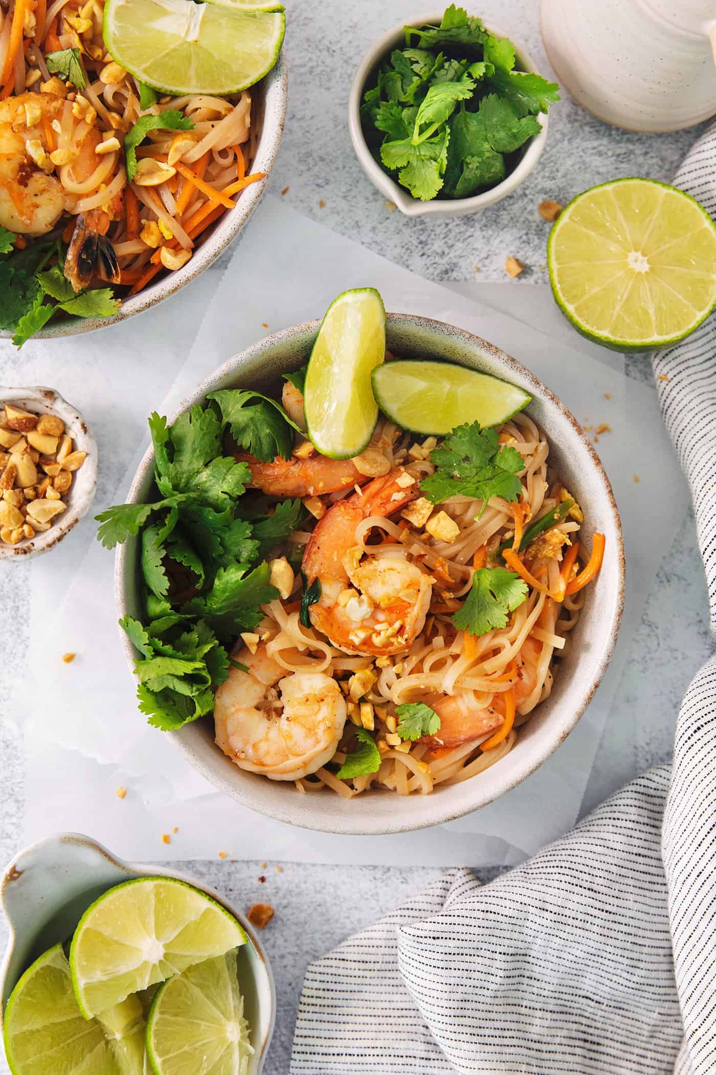An overhead shot of white bowls of shrimp pad Thai with bowls of lime wedges, on a white backgournd.