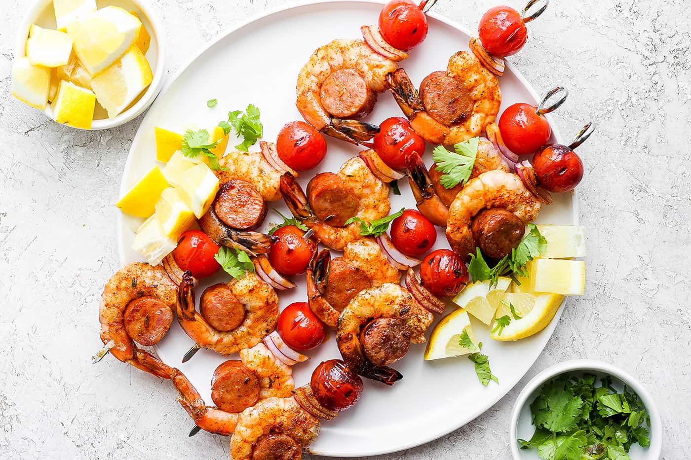 A white plate holds shrimp and sausage kabobs.