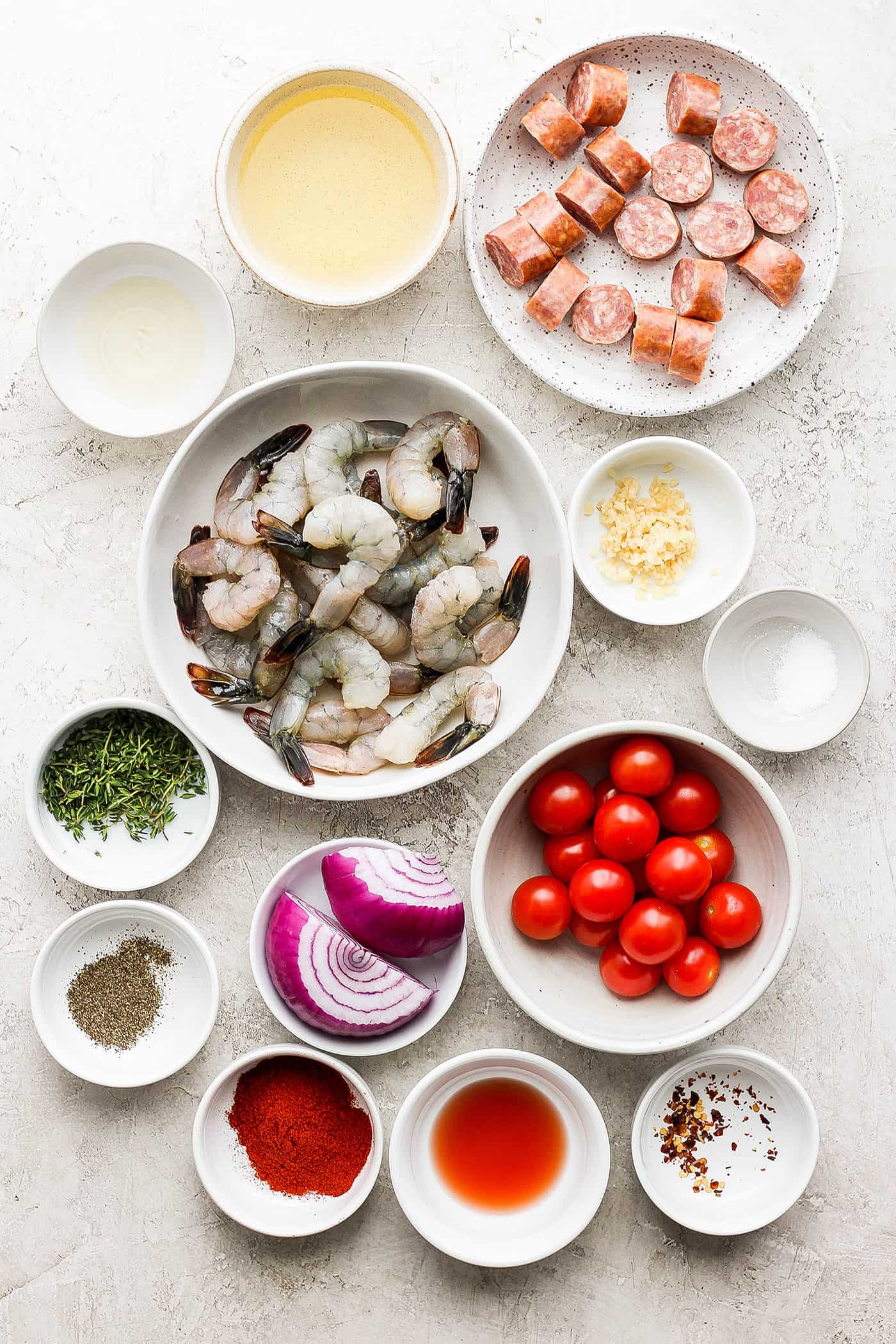 Bowls of ingredients for kabobs: tomatoes, shrimp, sausage, red onion, seasonings.