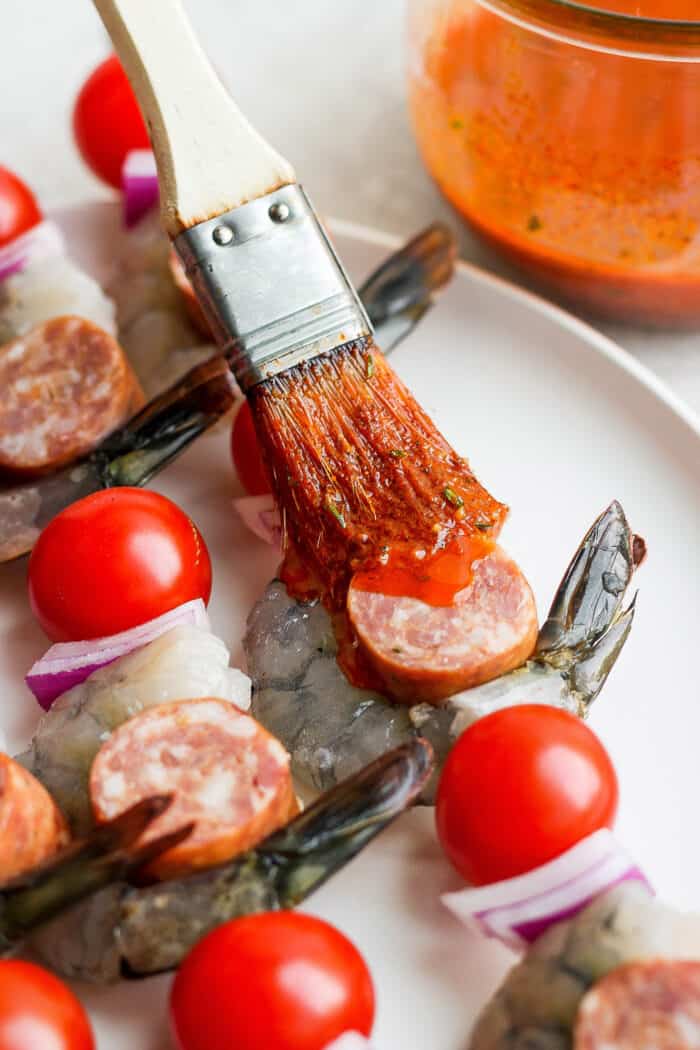 Brushing marinade onto shrimp and sausage kabobs.