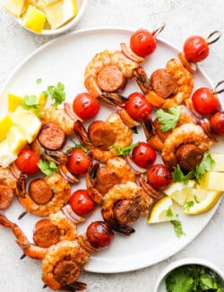 A white plate holds shrimp and sausage kabobs.