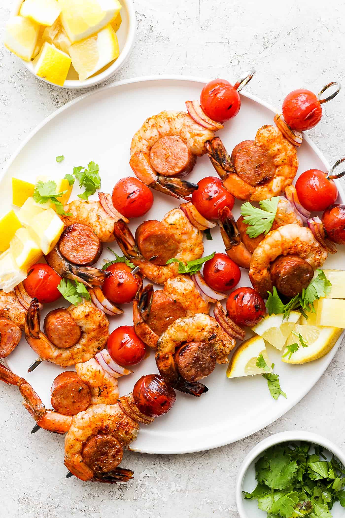 A white plate holds shrimp and sausage kabobs.