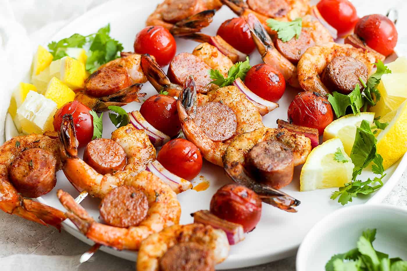 A white plate holds shrimp and sausage kabobs.