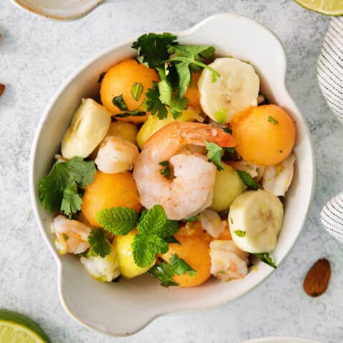 An overhead shot of a colorful bowl of tropical shrimp salad with fruit, shrimp, and mint leaves.