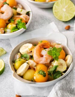 Bowls of colorful tropical shrimp salad are shown on a white background with limes.