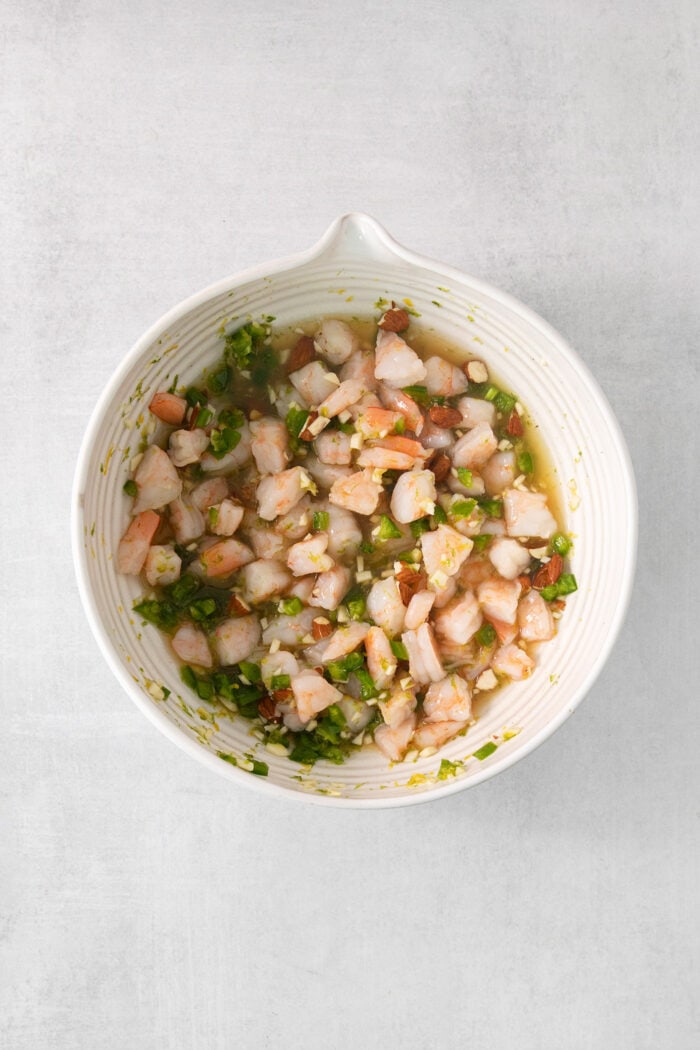 Shrimp is added to dressing in a white bowl to make tropical shrimp salad.