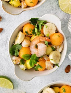 An overhead shot of a colorful bowl of tropical shrimp salad with fruit, shrimp, and mint leaves.