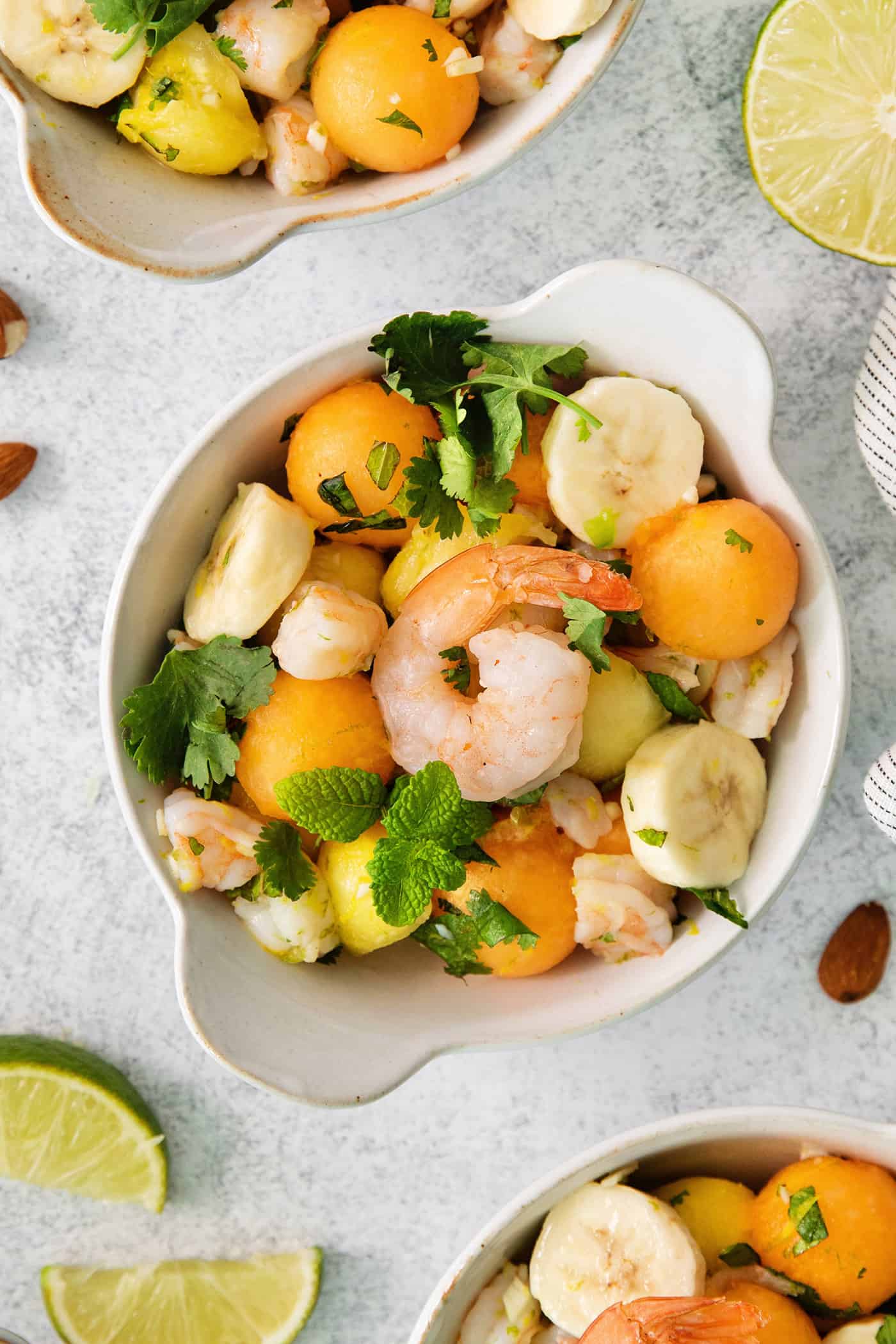 An overhead shot of a colorful bowl of tropical shrimp salad with fruit, shrimp, and mint leaves.