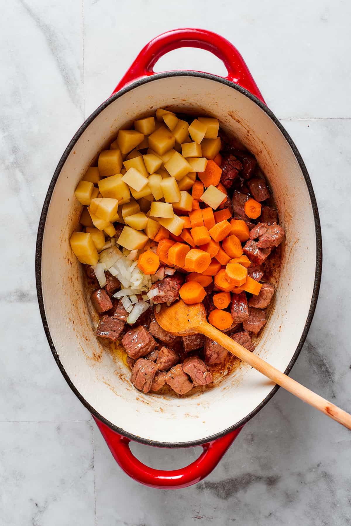 Meat and vegetables are shown added to a Dutch oven for beef pot pie.