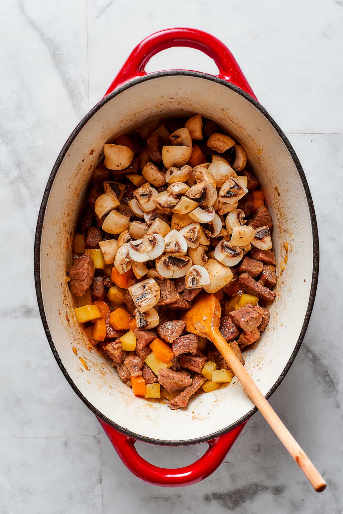 A wooden spoon stirs together ingredients in a Dutch oven for beef pot pie.