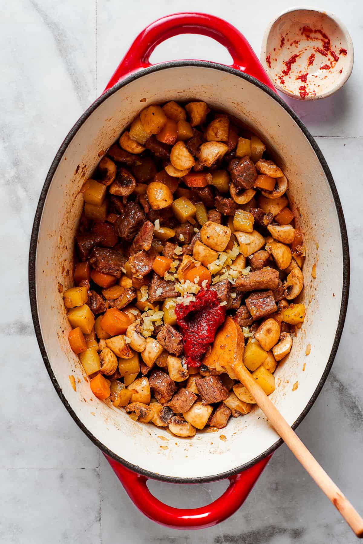 A wooden spoon stirs in tomato paste to a pot of beef pot pie filling.