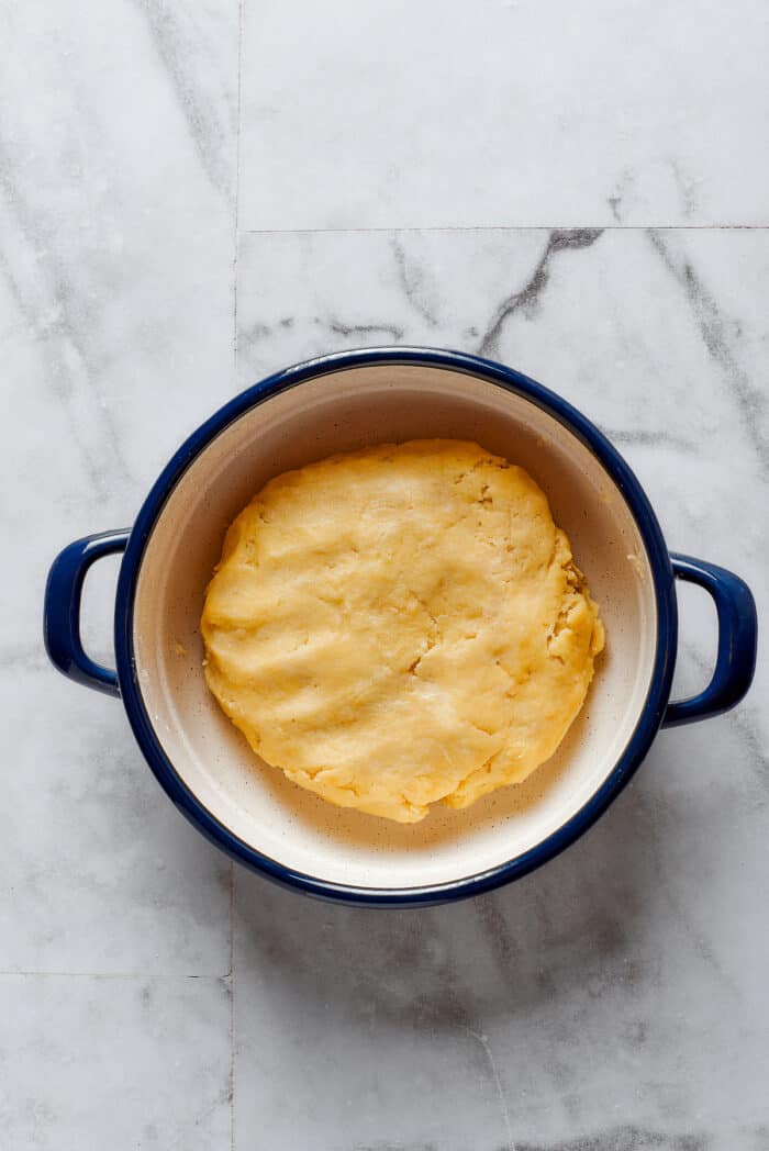 A ball of pie dough is seen in a pot.