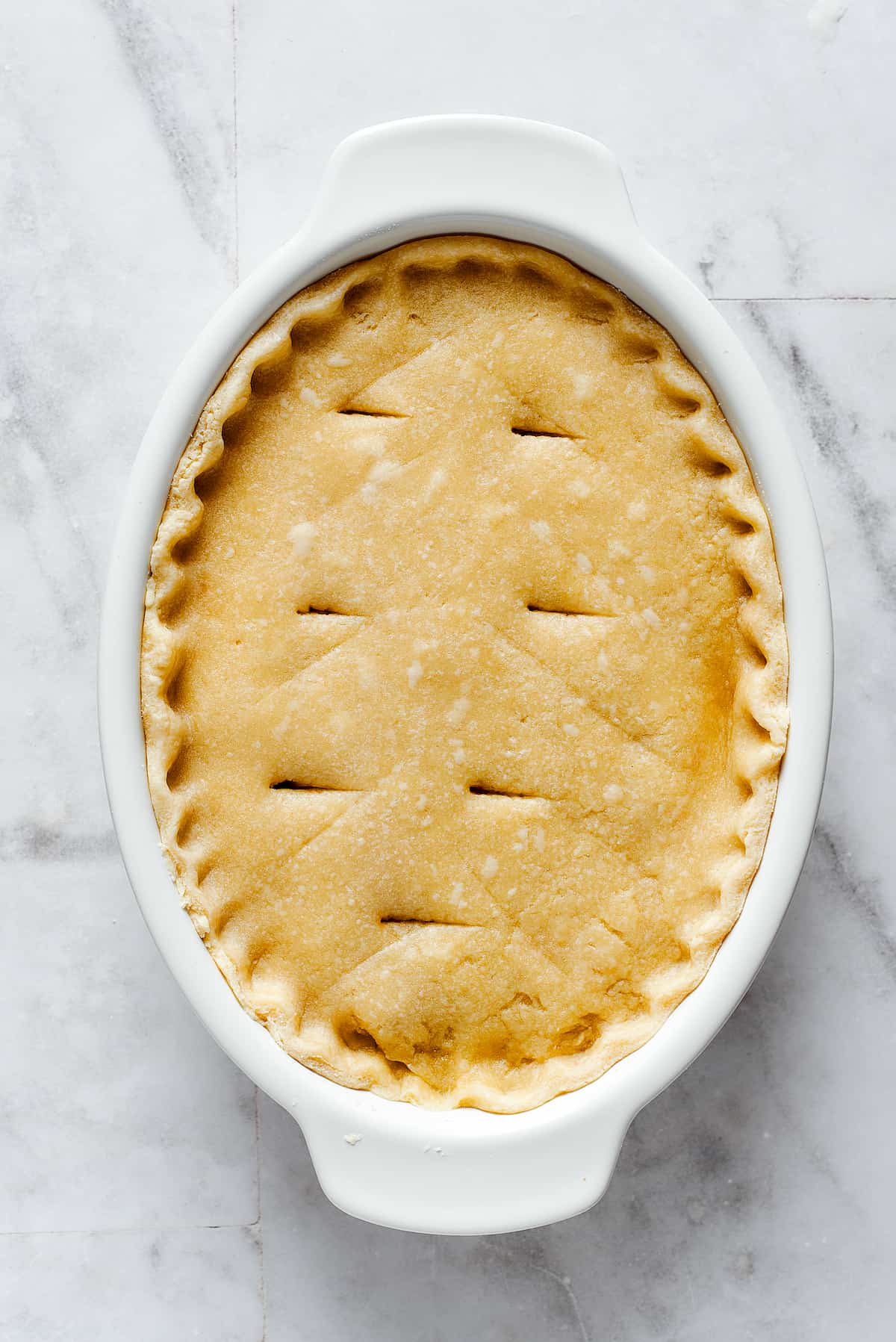 A white oval pie dish is topped with crust for pot pie filling.