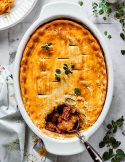 A beef pot pie is shown in a baking dish with a spoon.