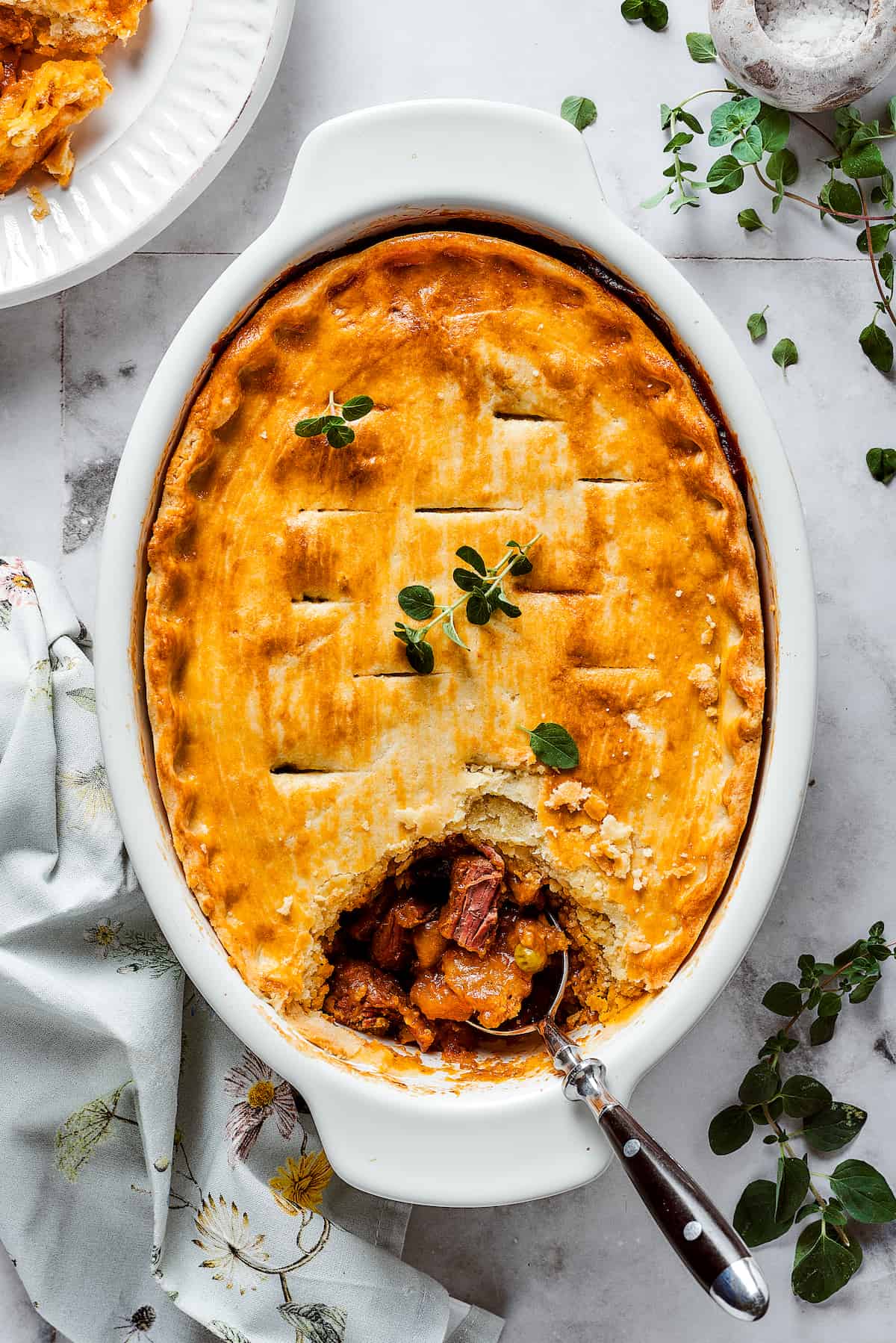 A beef pot pie is shown in a baking dish with a spoon.