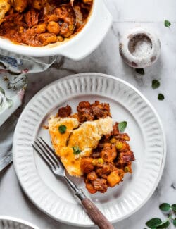 A plate of beef pot pie is shown with a fork and a dish of pot pie next to it.