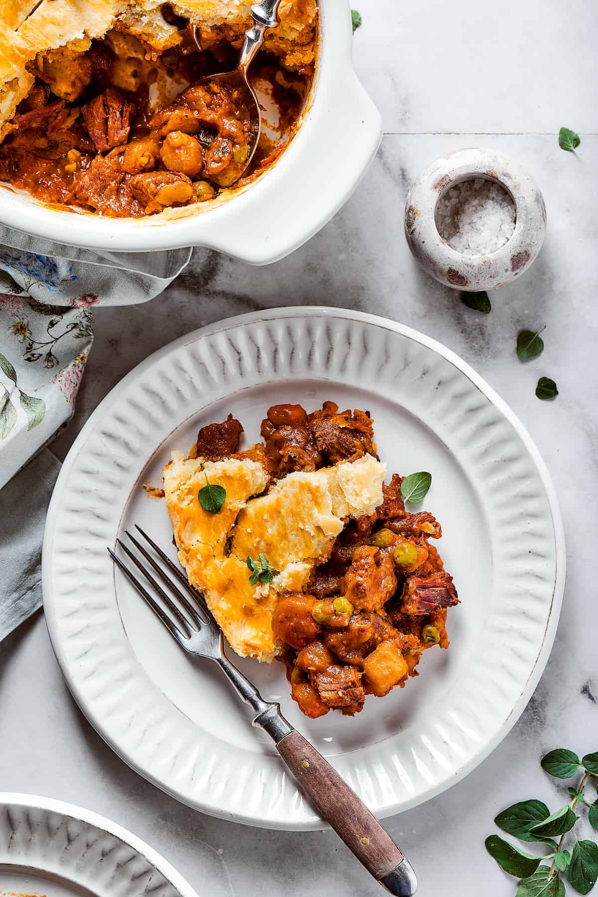 A plate of beef pot pie is shown with a fork and a dish of pot pie next to it.