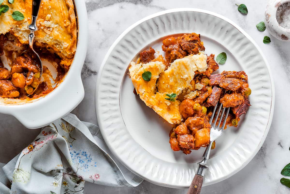 A plate of beef pot pie is shown with a fork and a dish of pot pie next to it.