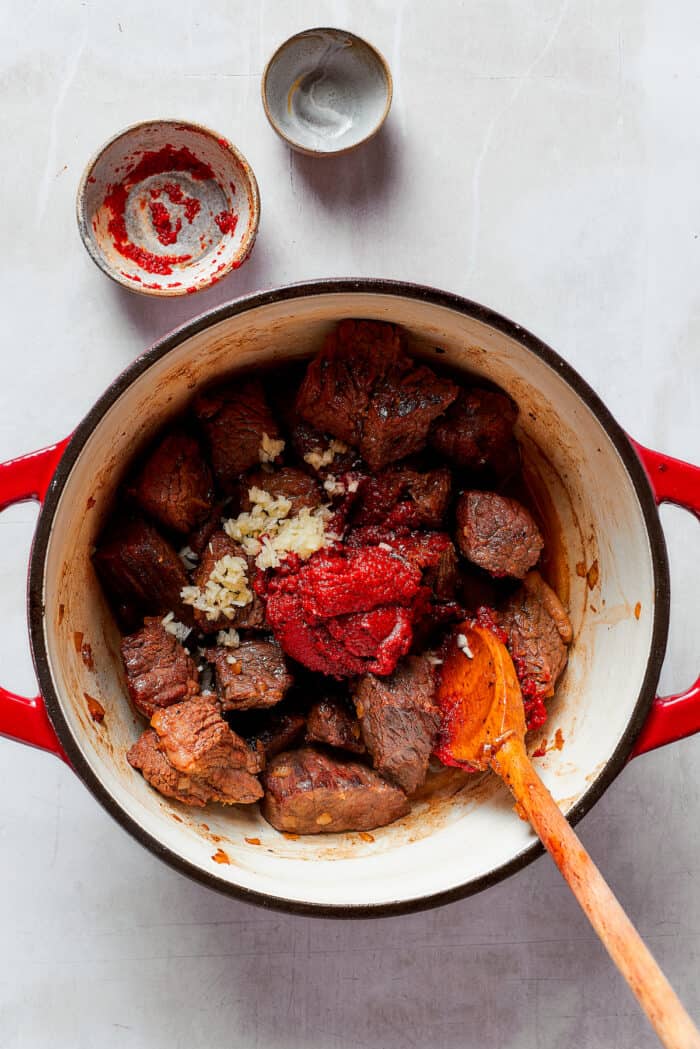 Tomato paste and garlic are added to a pot of Mulligan stew.