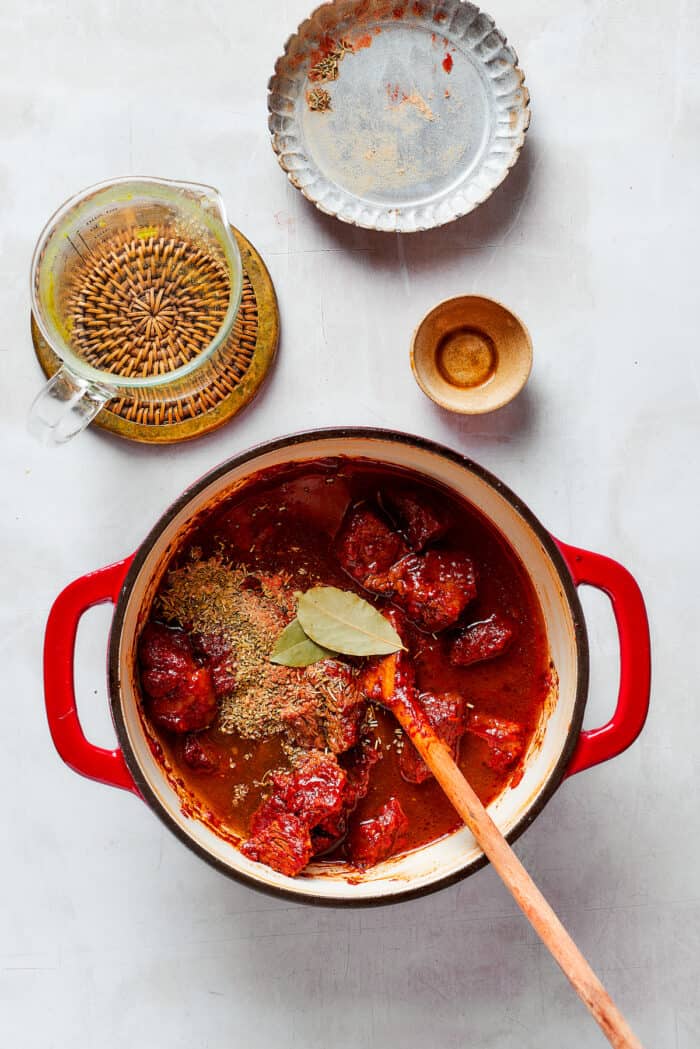 A pot of Mulligan stew and a wooden spoon are shown with beef broth and bay leaves.