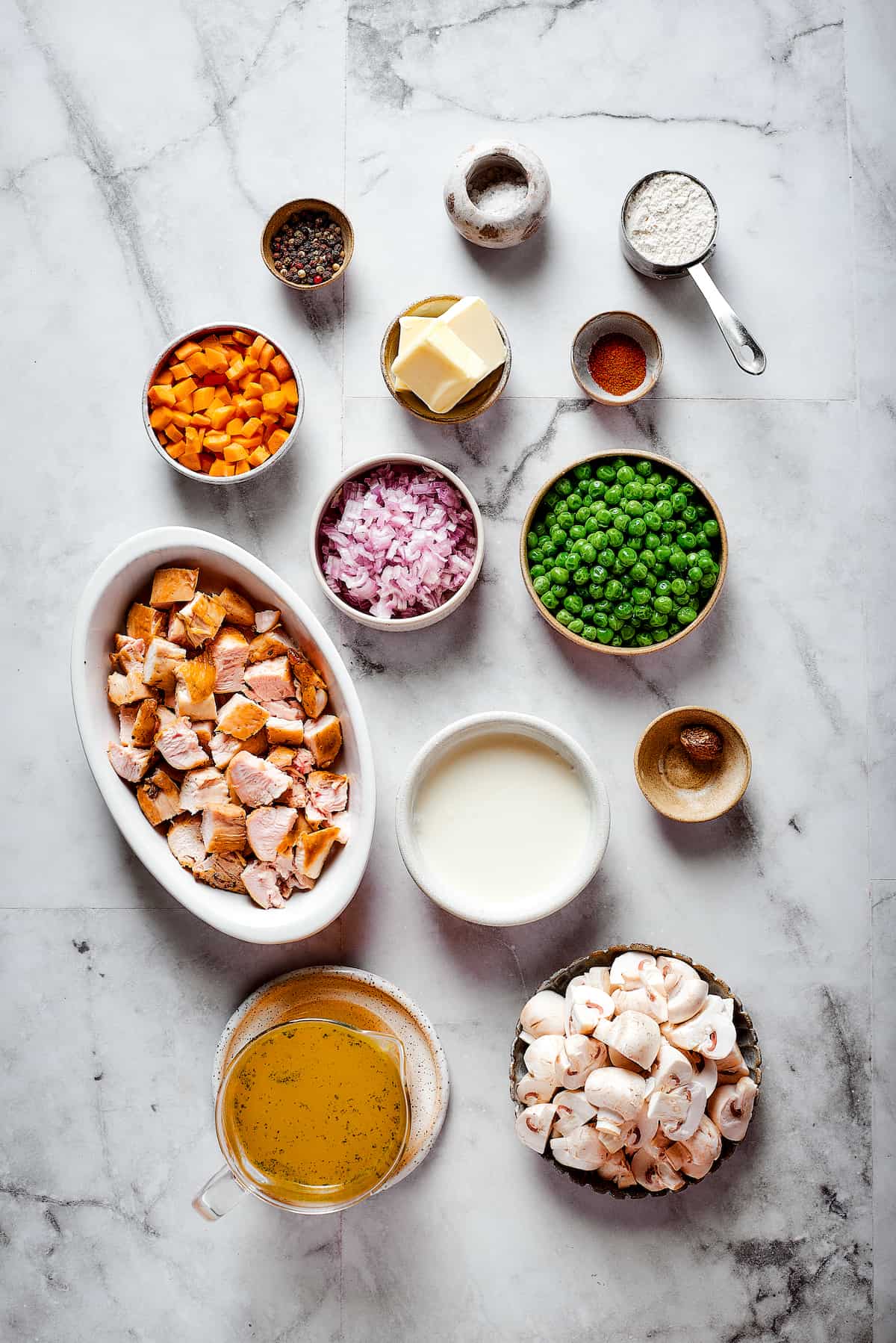 The ingredients for Turkey a La King are shown portioned out: on a white background: peas, turkey, butter, carrots, salt, pepper, paprika, and mushrooms.