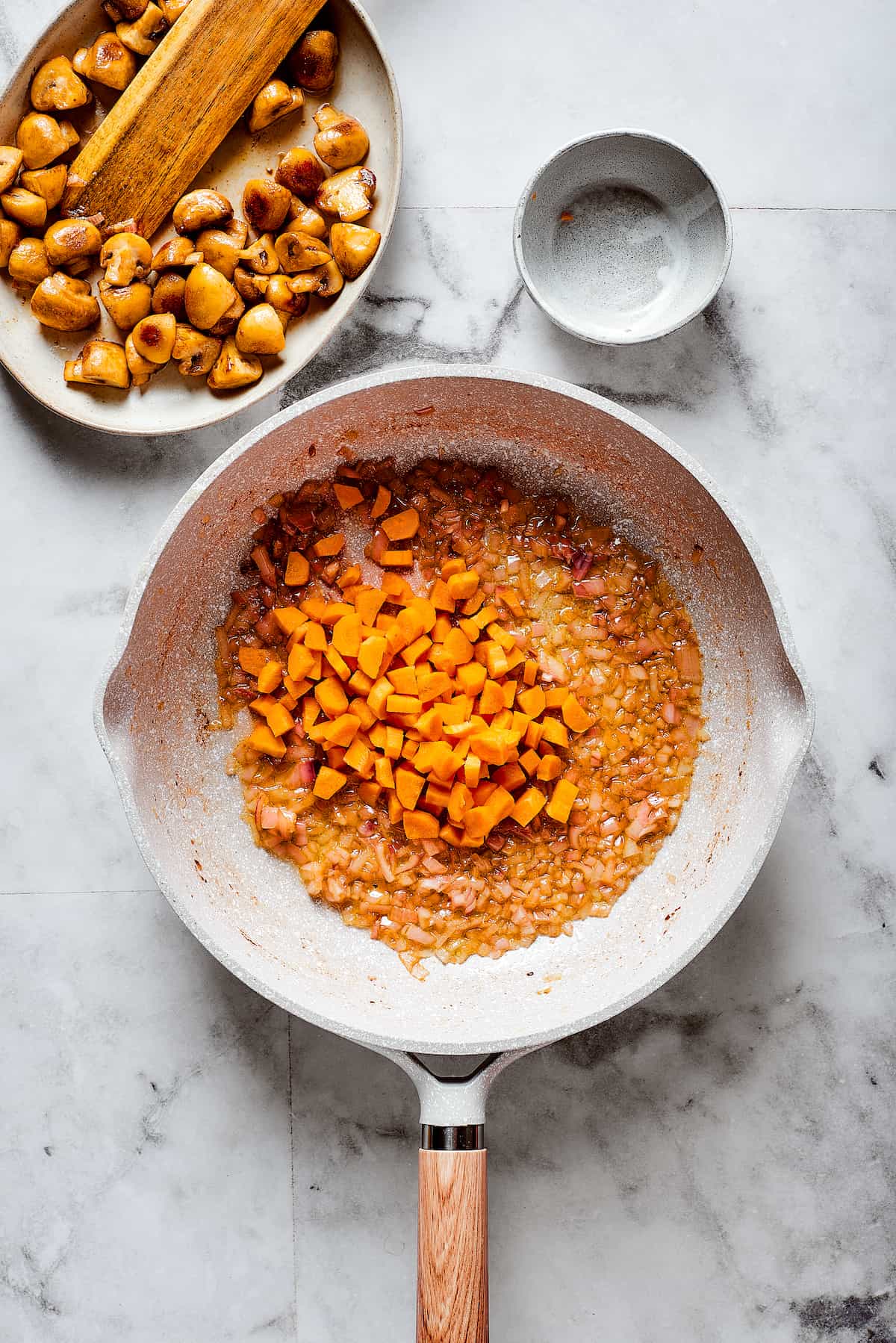 Carrots are added to a pan of mushrooms.